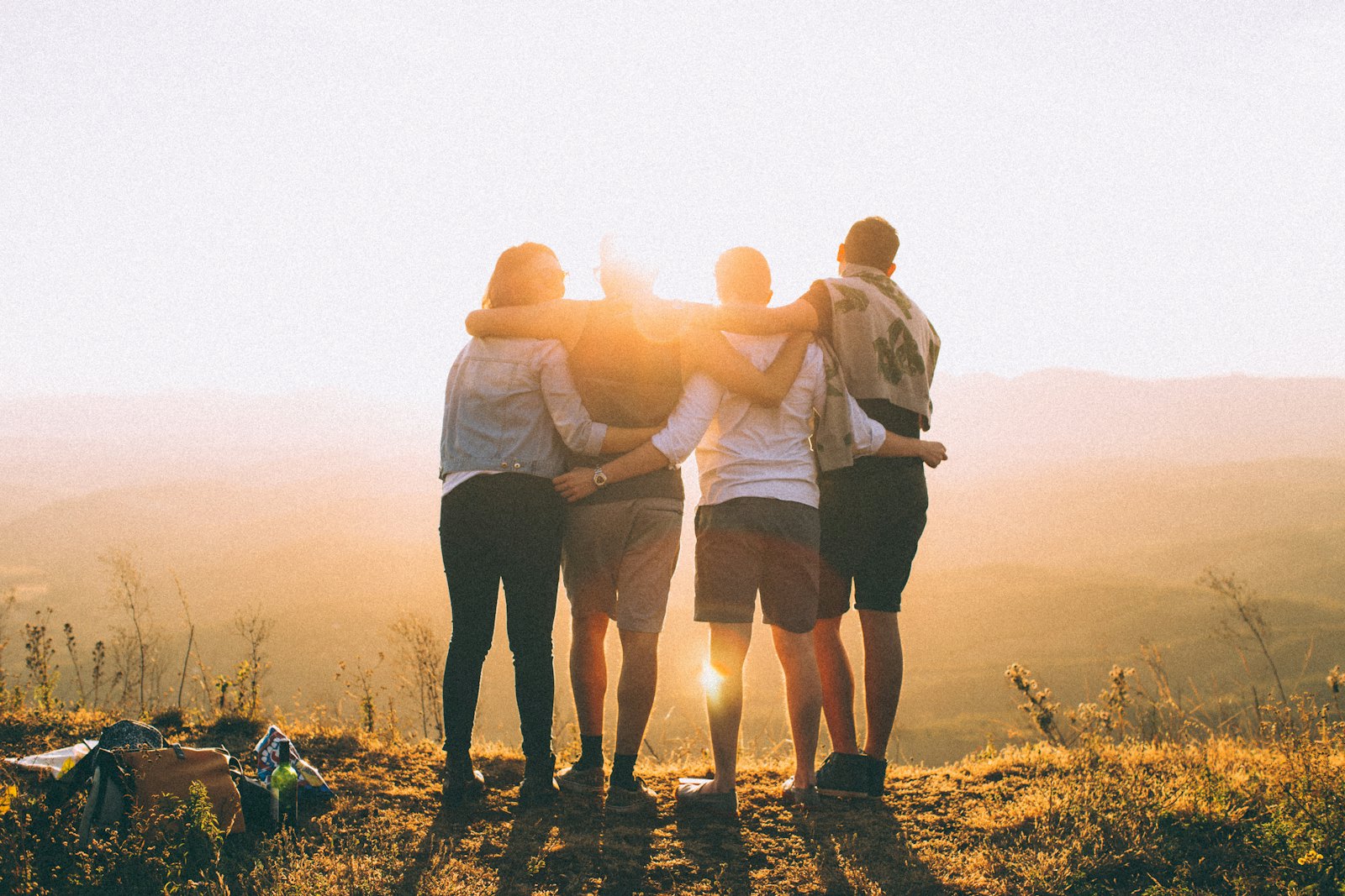 Quatre amis de dos, sacs à dos posés, devant une vallée au coucher du soleil